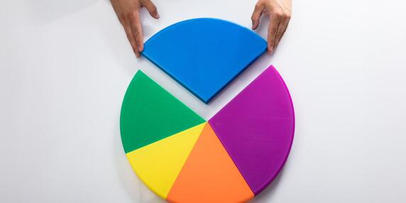 Zwei Hände fügen das letzte blaue Segment in ein fünfteiliges, buntes Kreisdiagramm ein. Die anderen Segmente sind grün, gelb, pink und lila.